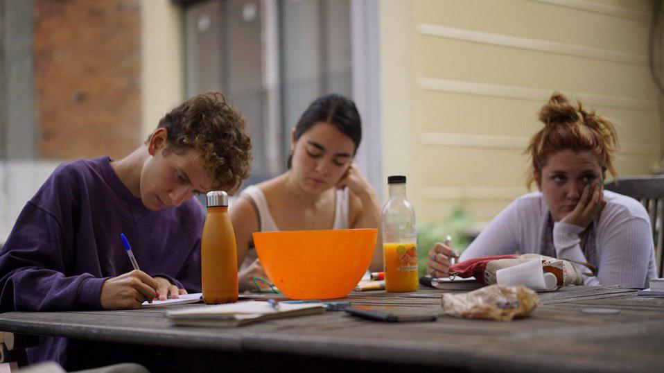 Tres personas jóvenes concentradas sentadas alrededor de una mesa con comida y material para escribir