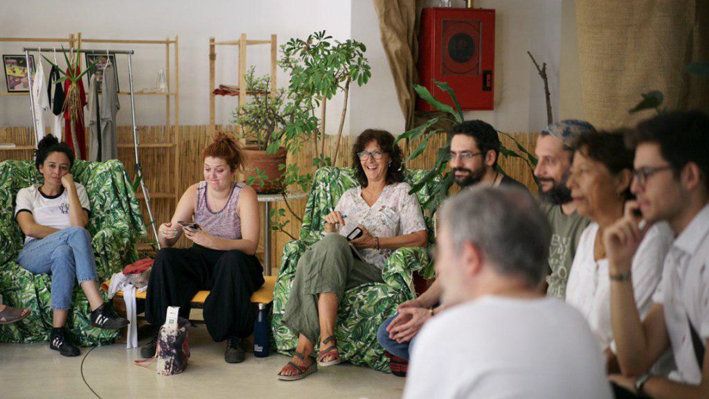 Grupo de gente sentada en círculo en una sala con plantas. Se están divirtiendo.
